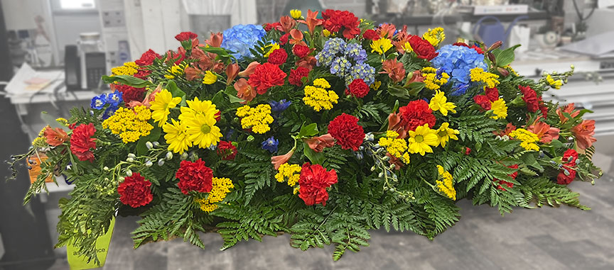 Casket spray with yellow, red, and blue flowers.