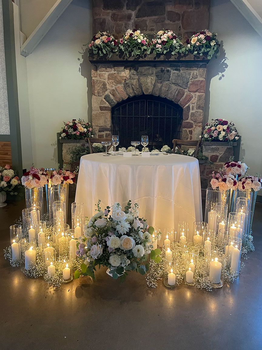 Bridal party table decorated with floral arrangement and candles.